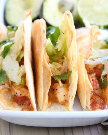 three crispy shrimp tacos in flour tortillas with lettuce on white tray