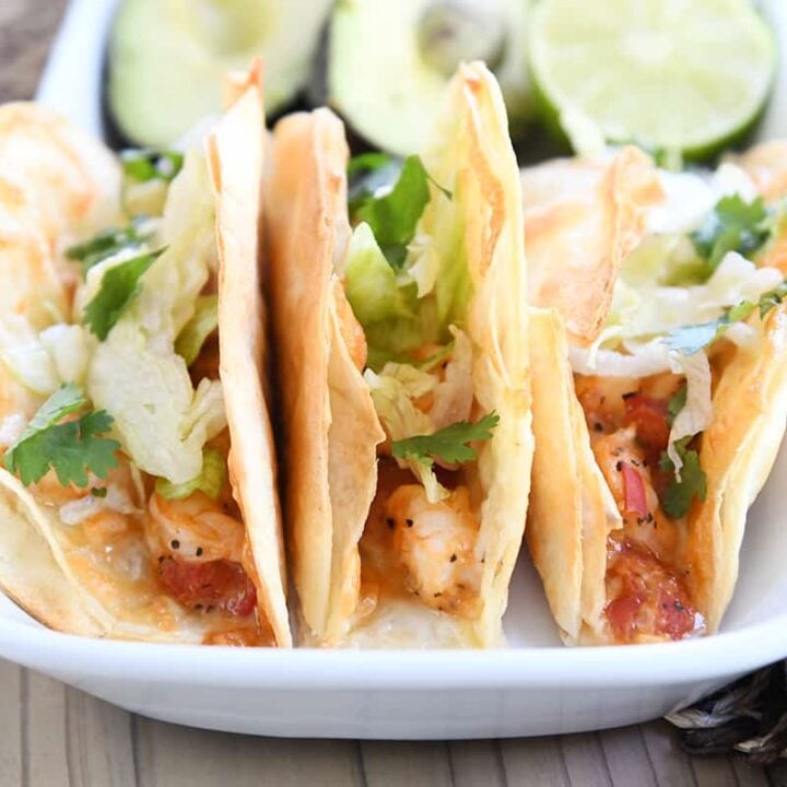 three crispy shrimp tacos in flour tortillas with lettuce on white tray