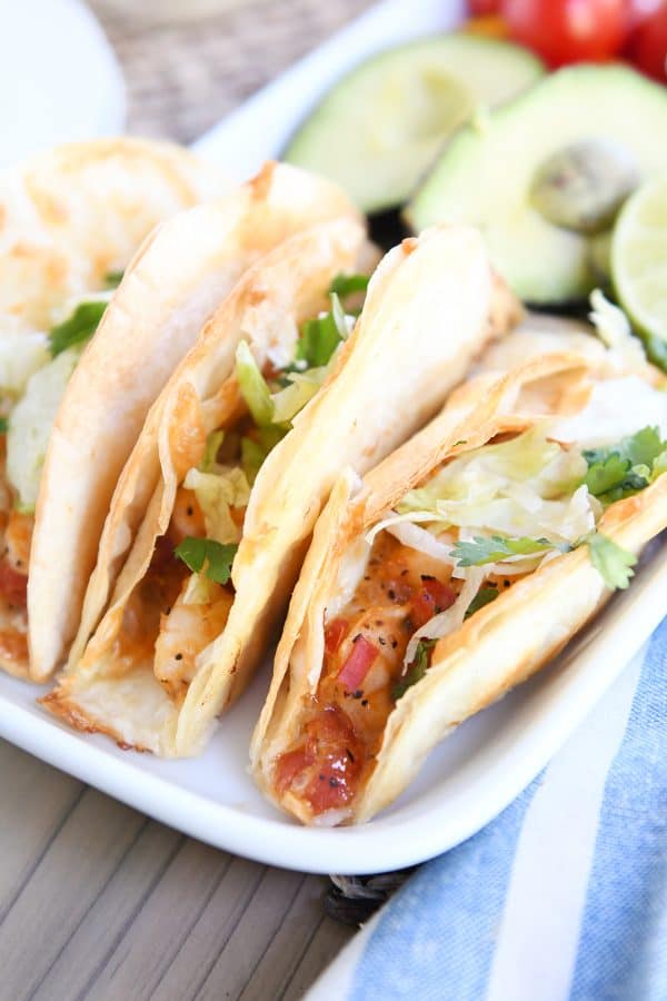 Three crispy shrimp tacos with lettuce on white tray.