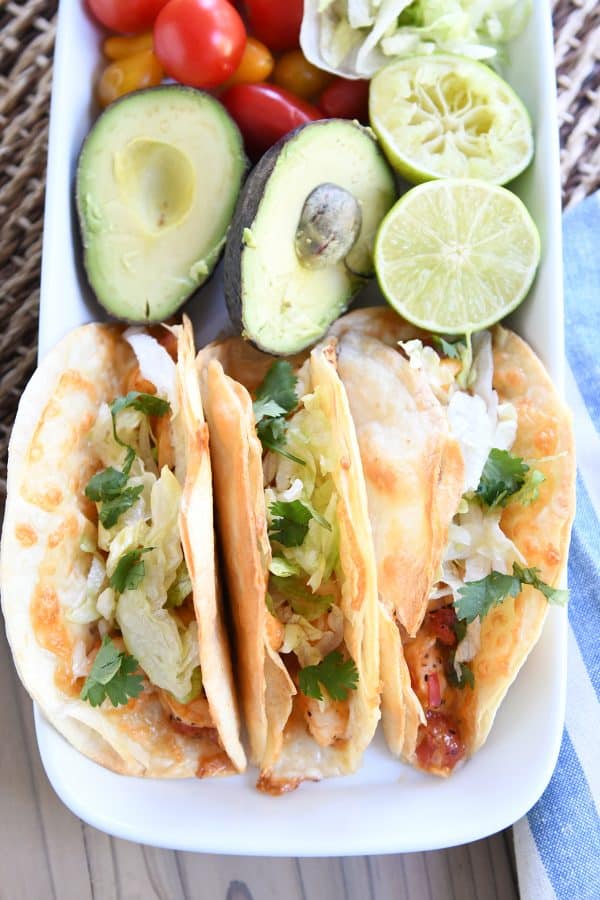 Top down view of a tray of shrimp tacos, an avocado cut in half, and a lime cut in half.