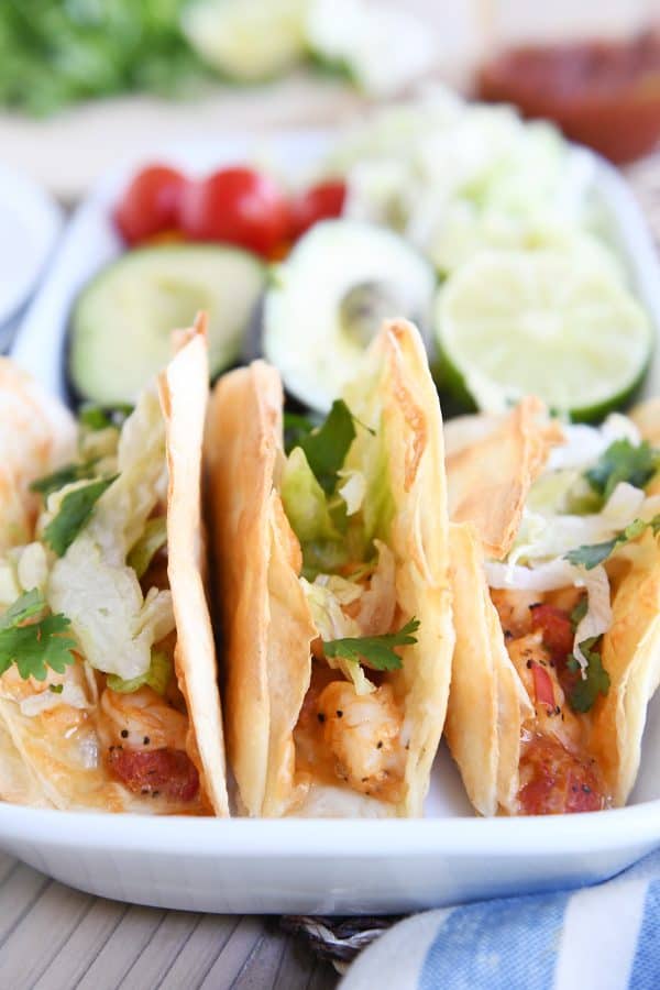 Three crispy shrimp tacos with lettuce on white tray.