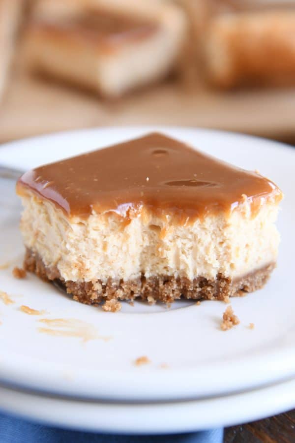 Dulce de leche cheesecake square on white plate with bite taken out.