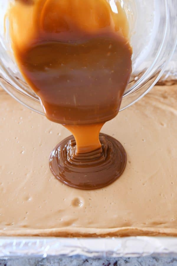 Pouring dulce de leche on top of baked cheesecake bars.