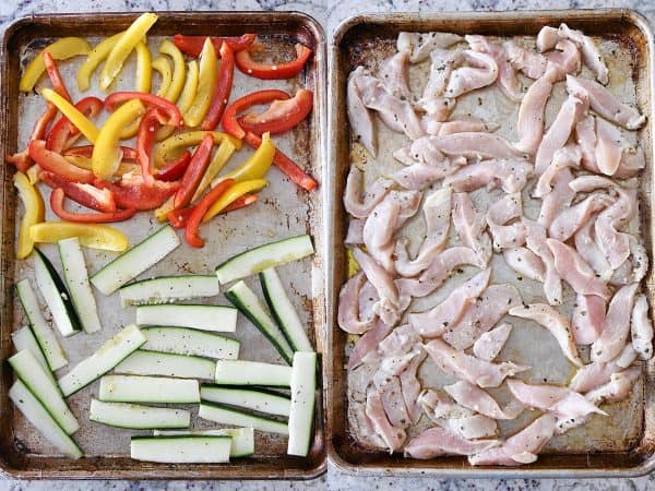 Zucchini and bell peppers and marinated chicken on sheet pans.