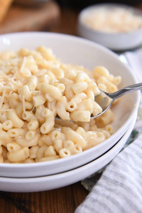 Spoon scooping up mac and cheese in white bowl.