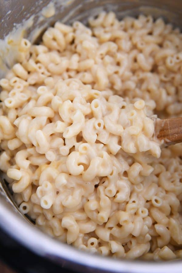 Stirring mac and cheese in pressure cooker with wooden spoon.