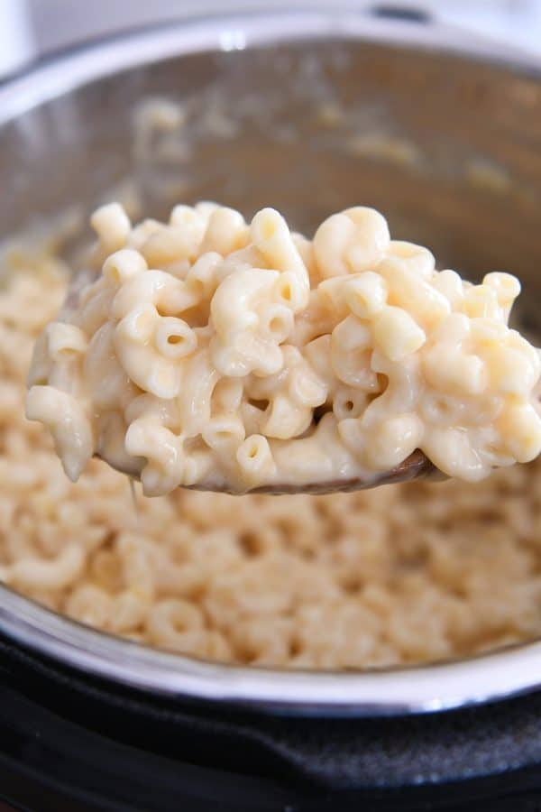 Scooping up warm pressure cooker mac and cheese on wooden spoon.