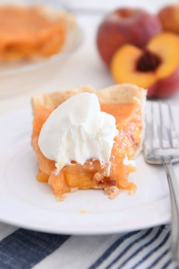 Slice of fresh peach pie on white plate with bite taken out.