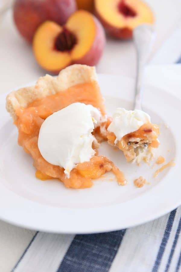 Bite of fresh peach pie on fork on white plate.