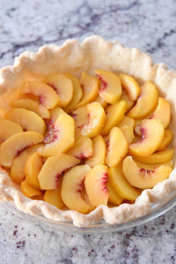 Baked pie shell with sliced fresh peaches evenly placed on the bottom.