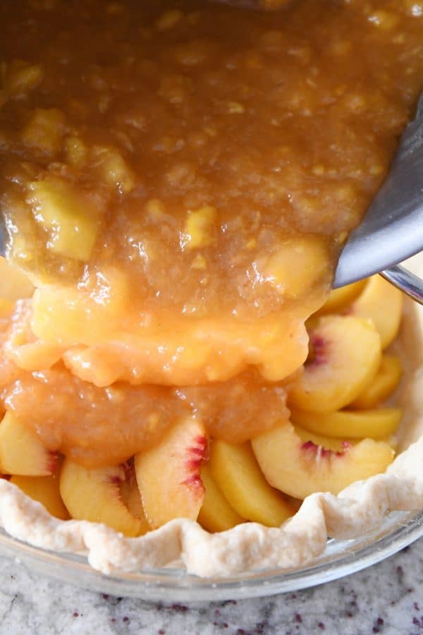 Pouring peach pie filling into pie.