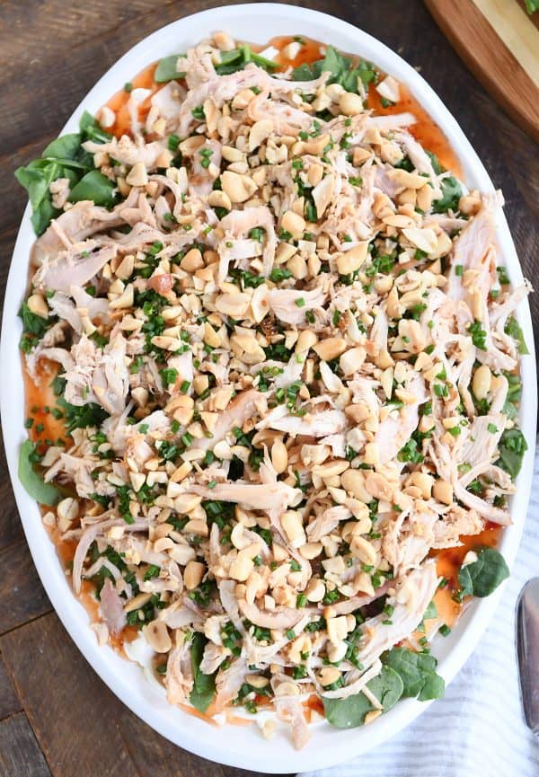 Top down view of white platter topped with cream cheese, sweet Thai chili sauce, spinach, shredded chicken, chives and peanuts.