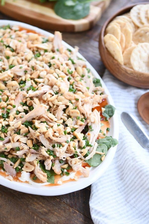 White platter of sesame Thai chicken dip in view with rice crackers in wood bowl.