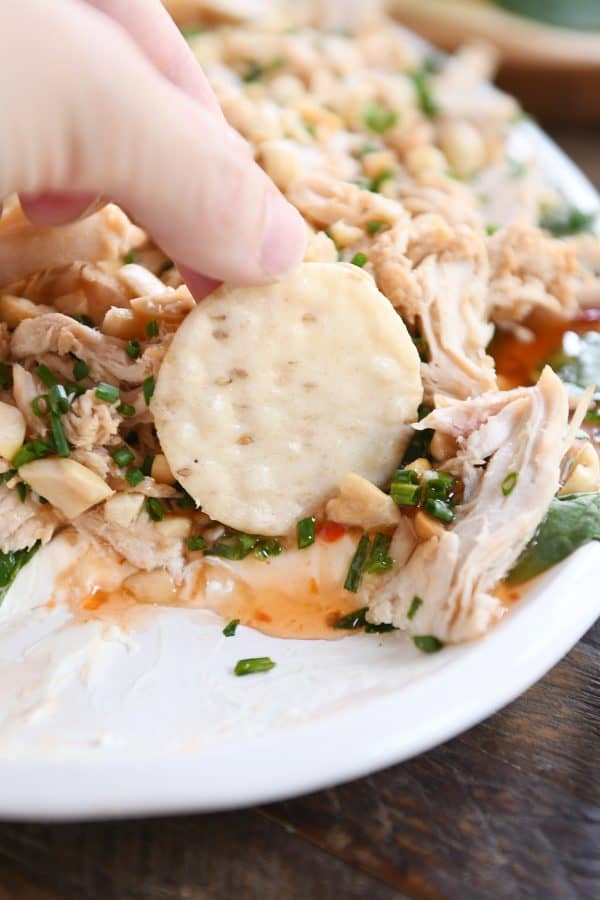 dipping rice cracker into 5-layer sesame Thai chicken dip on white platter