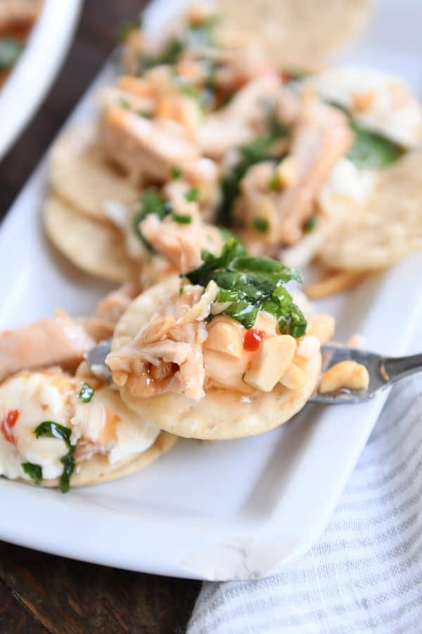 Small white tray with rice crackers and cream cheese, sweet Thai chili sauce, spinach and peanuts.