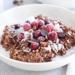 double chocolate steel cut oats in white bowl with coconut, chocolate chips and raspberries