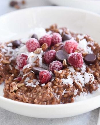 double chocolate steel cut oats in white bowl with coconut, chocolate chips and raspberries