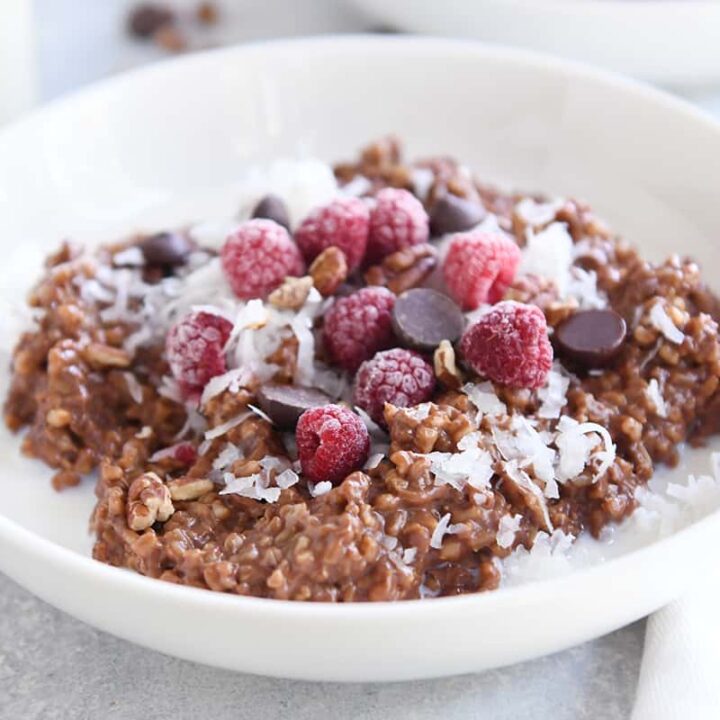 double chocolate steel cut oats in white bowl with coconut, chocolate chips and raspberries