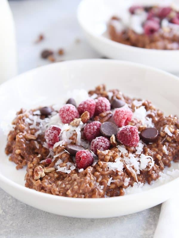 Double chocolate steel cut oats in white bowl with coconut, chocolate chips and raspberries.