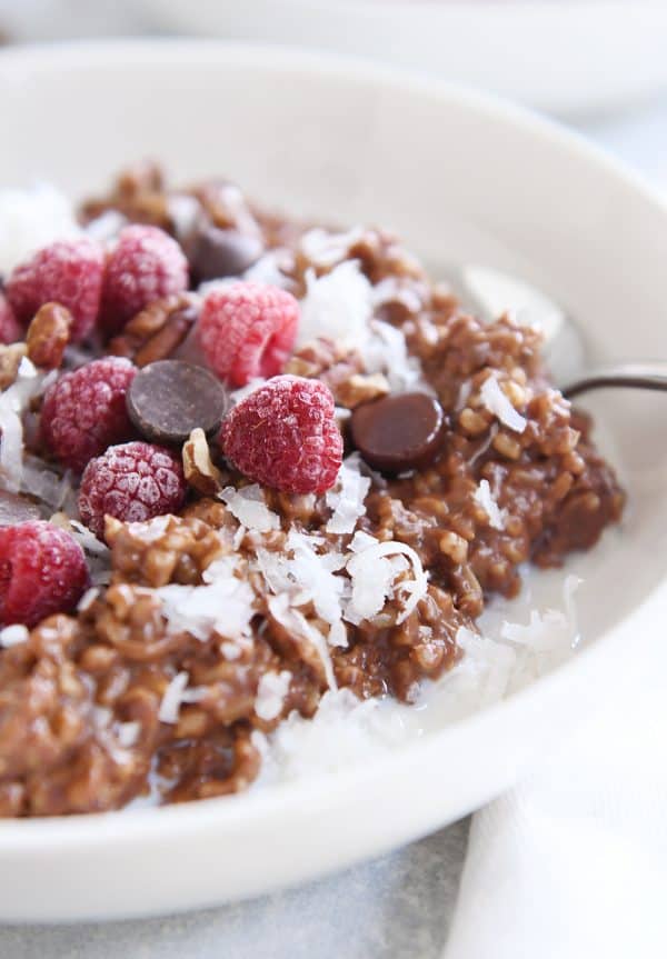 Instant pot chocolate steel cut oats in white bowl with chocolate chips and frozen raspberries.