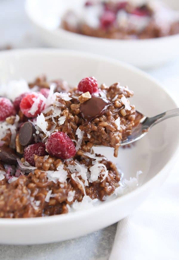 Scooping spoonful of chocolate steel cut oats with coconut and raspberries in white bowl.