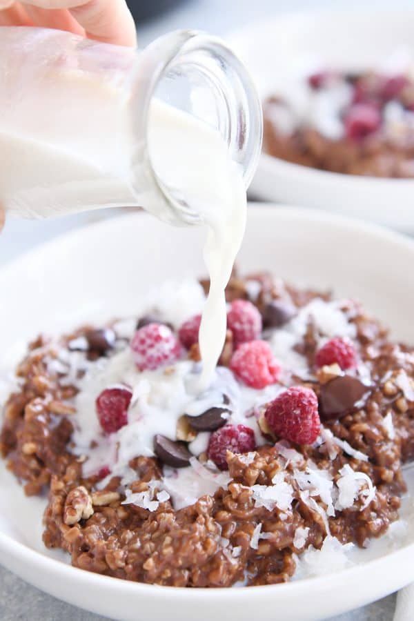 pouring milk over instant pot chocolate steel cut oats in white bowl with frozen raspberries