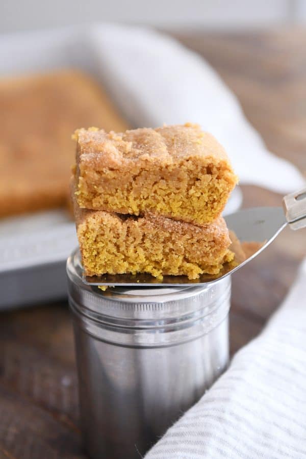 Two pumpkin snickerdoodle bars stacked on top of cinnamon and sugar canister.