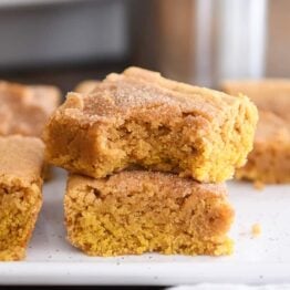 two pumpkin snickerdoodle bars stacked on white tray with bite taken out of top bar