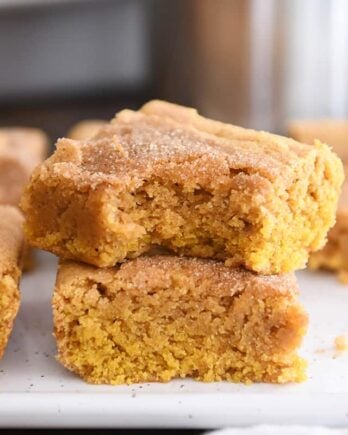 two pumpkin snickerdoodle bars stacked on white tray with bite taken out of top bar