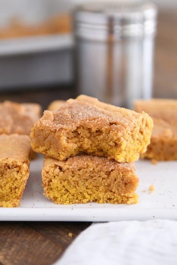 Two pumpkin snickerdoodle bars stacked on white tray with bite taken out of top bar.