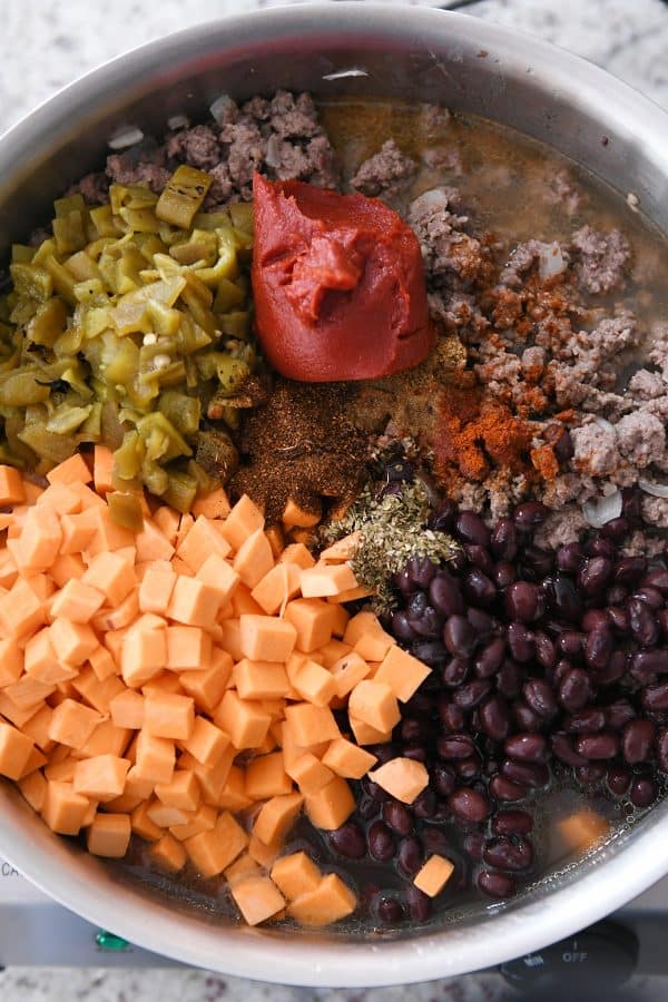 Skillet with sweet potatoes, green chiles, tomato paste, ground beef and black beans.