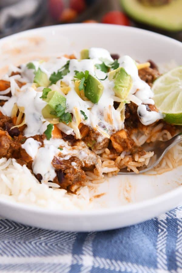 Scooping out bites of skillet sweet potato black bean burrito bowl ingredients in white bowl.