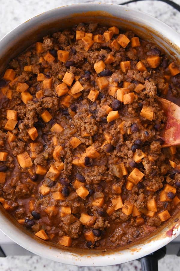 Wooden spoon in skillet with sweet potato black bean burrito filling.