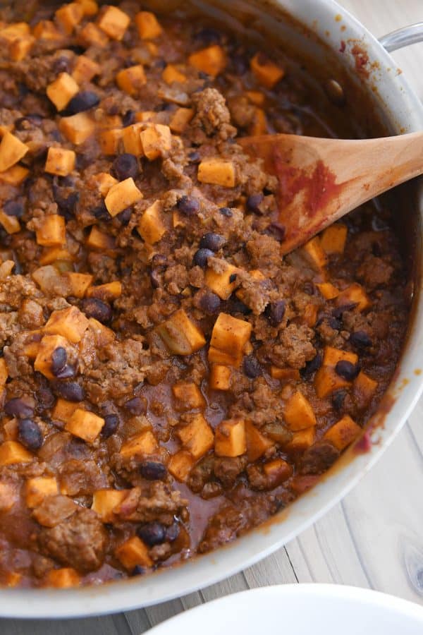 Wooden spoon in skillet with sweet potato black bean burrito filling.