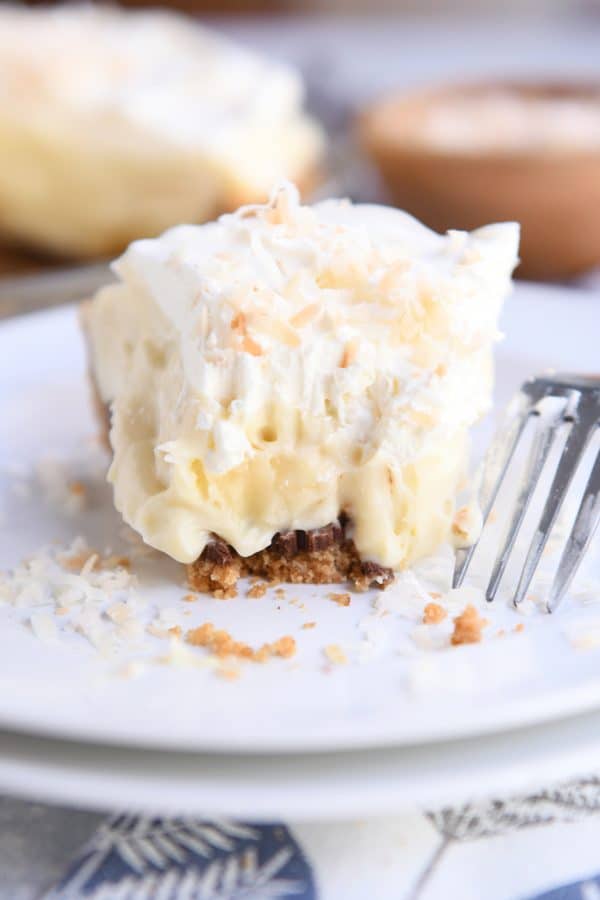 bite taken out of banana coconut cream pie on white plate with fork