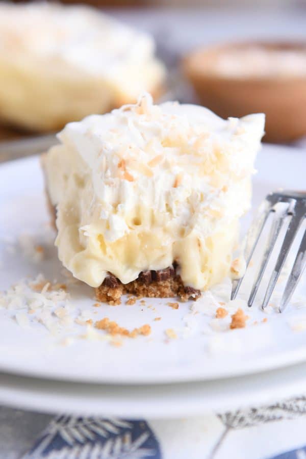 Bite taken out of banana coconut cream pie on white plate with fork.