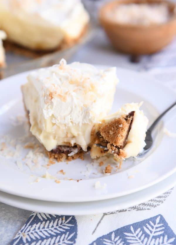 bite of banana coconut cream pie on fork on two white stacked plates