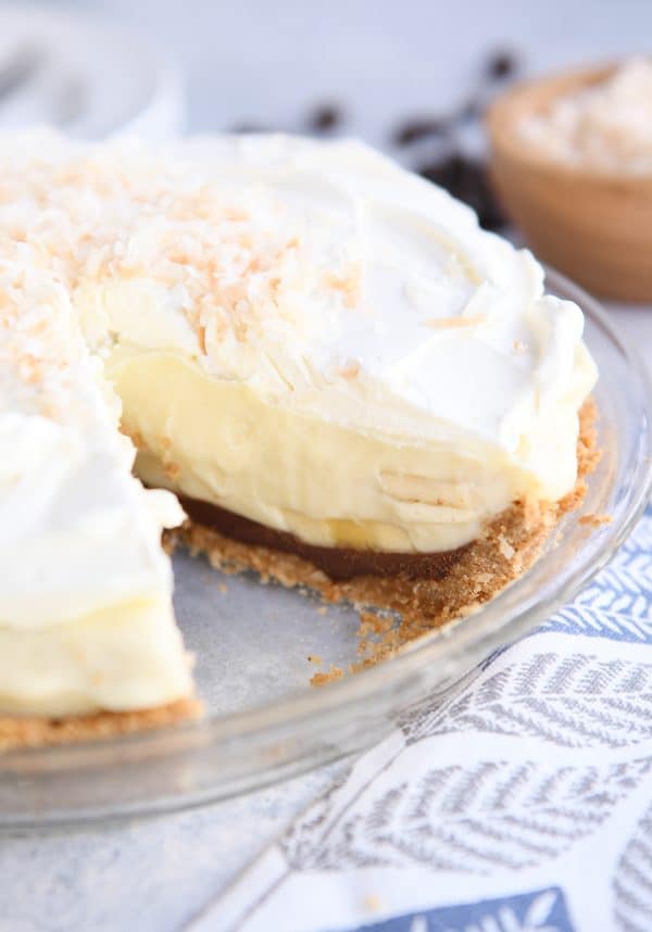 whole banana coconut cream pie in glass pie plate with piece removed