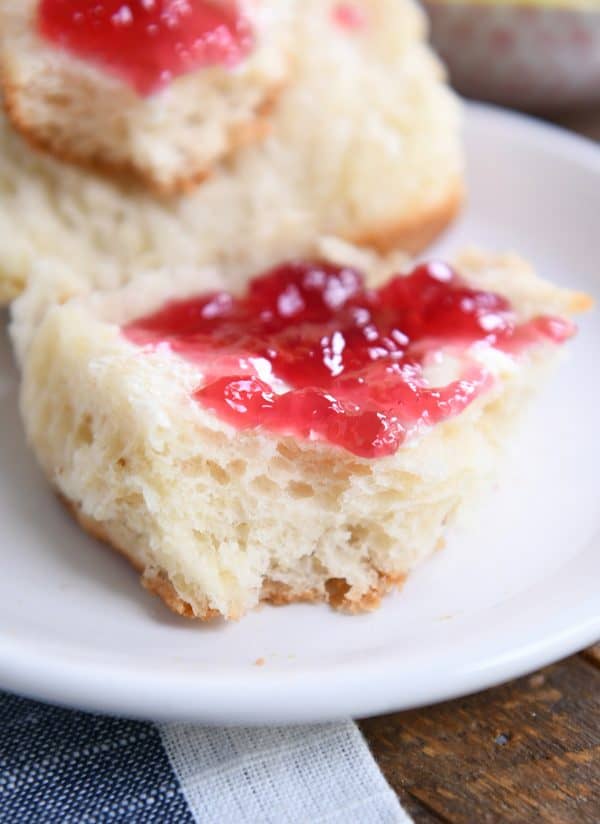 Close up view of super fluffy dinner roll with butter and jam on white plate.