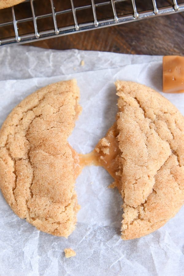 one brown butter caramel snickerdoodle in half pulled apart with caramel stretching on white parchment