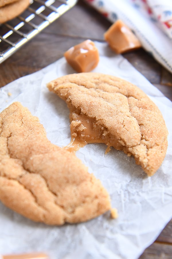 One brown butter caramel snickerdoodle in half pulled apart with caramel stretching on white parchment.