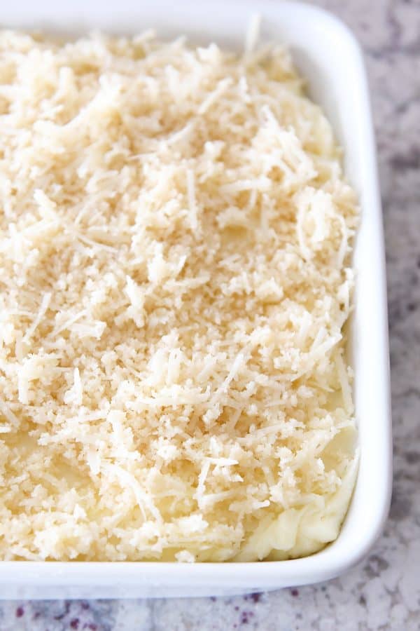 Mashed potatoes in white dish topped with buttery parmesan and bread crumb topping.