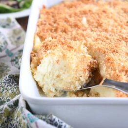 metal spoon scooping out spoonful of baked mashed potatoes with parmesan topping in white dish