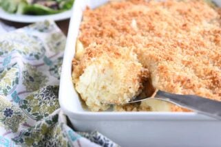 metal spoon scooping out spoonful of baked mashed potatoes with parmesan topping in white dish