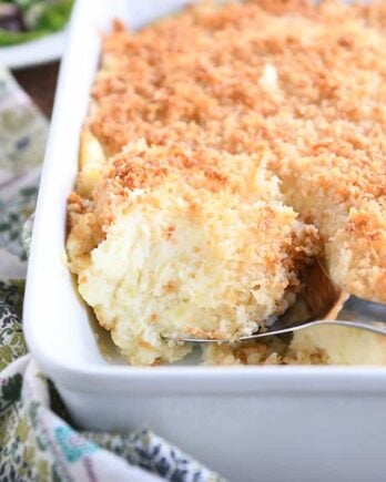 metal spoon scooping out spoonful of baked mashed potatoes with parmesan topping in white dish