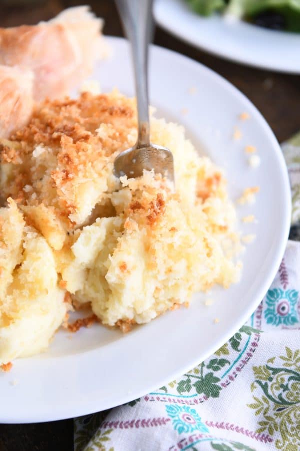 Fork scooping off part of creamy baked mashed potatoes on white plate.