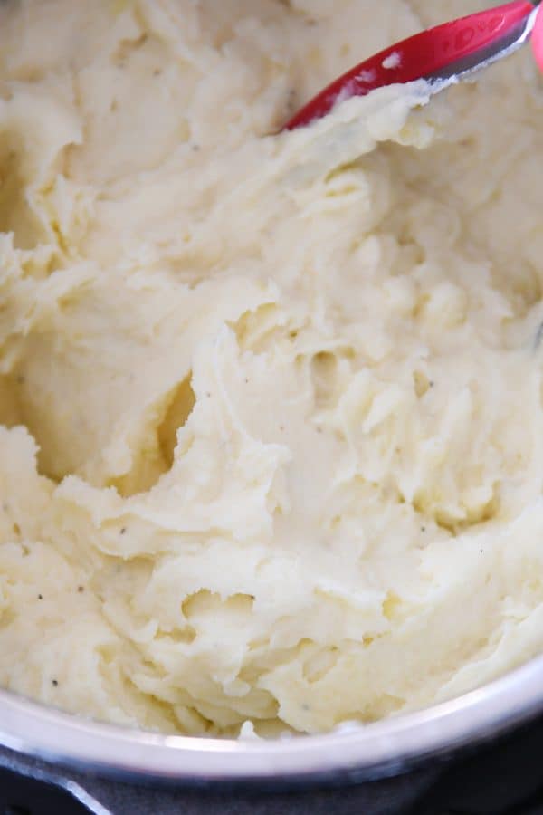 Creamy mashed potatoes in instant pot with potato masher.