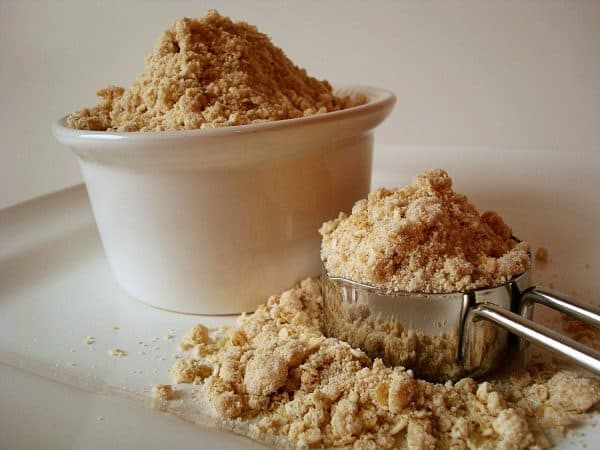 A white bowl and metal measuring cup full of oatmeal pancake mix. 