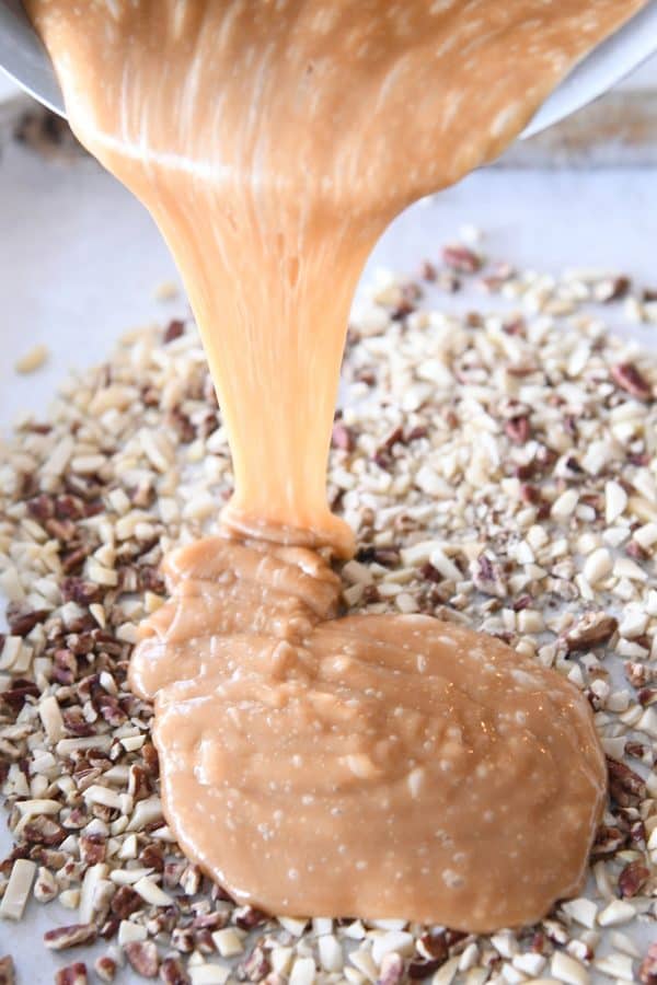 Pouring homemade toffee over chopped nuts on sheet pan.