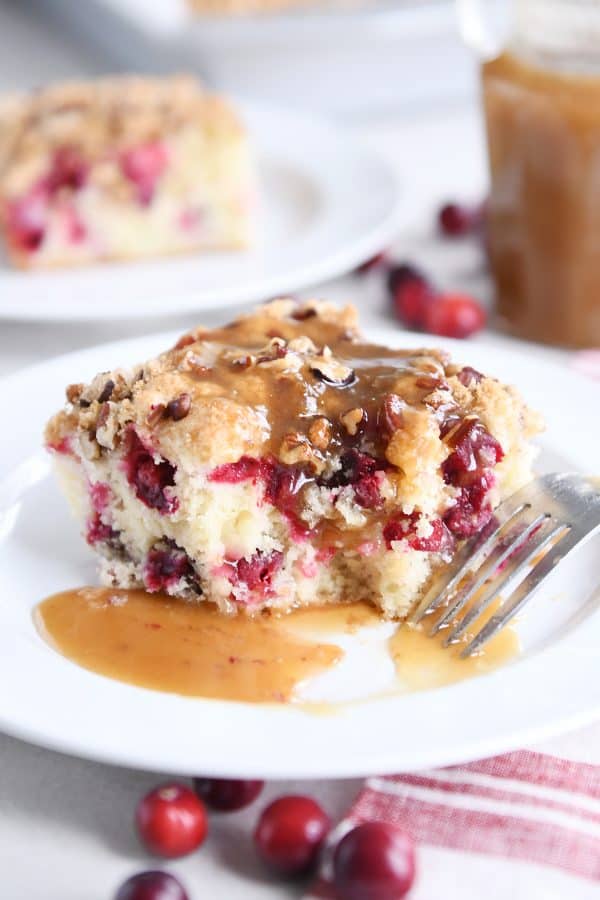 Piece of cranberry coffee cake with warm vanilla sauce on white plate.